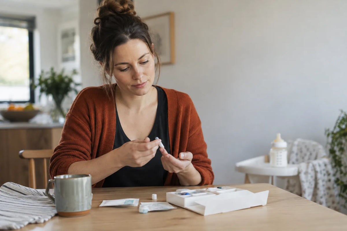 New mother with an at-home kit to check hormone levels postpartum in a bright kitchen