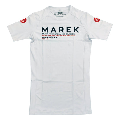 A white short-sleeve athletic jersey with 'MAREK' printed in black across the chest, accompanied by smaller black and red text. The jersey features red circular logos on both shoulders and a small green brand label inside the collar.